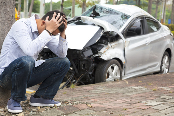 man with head in hands by crashed car